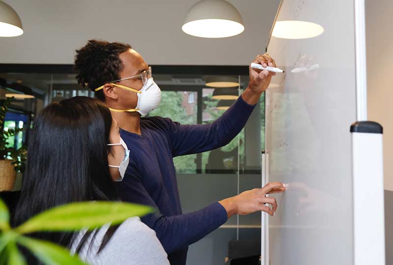 Employees work together on a project while wearing masks during phase two